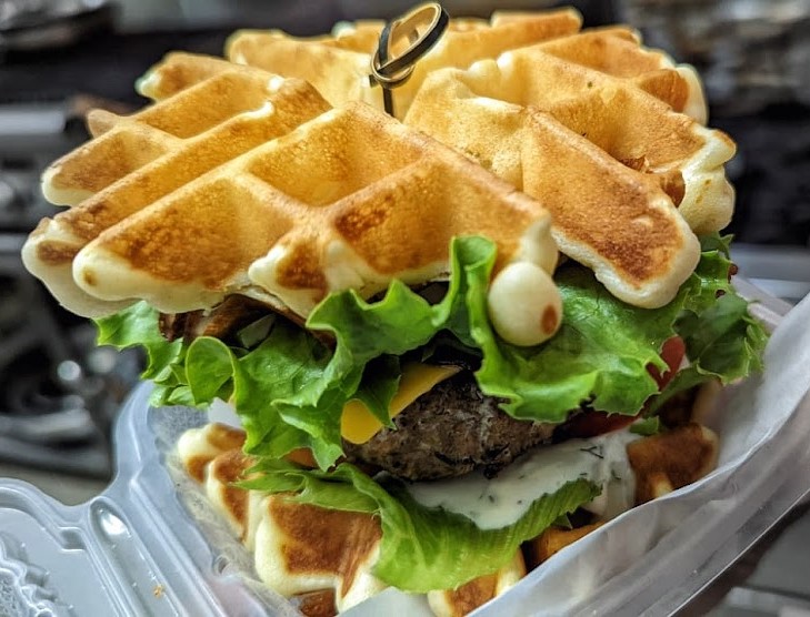 Fried chicken waffle sandwich with lettuce, tomato, cheese, and ranch